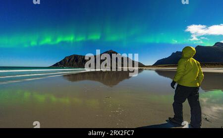 Einsamer Wanderer, der die Berge und das kalte arktische Meer unter den Nordlichtern (Aurora Borealis), den Strand von Skagsanden und Ramberg bewundert Stockfoto