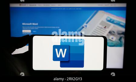 Person, die ein Smartphone mit dem Logo der Textverarbeitungssoftware Microsoft Word auf dem Bildschirm vor der Website hält. Konzentrieren Sie sich auf das Display des Telefons. Stockfoto