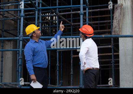 Zwei Architekten tragen einen Schutzhelm und sprechen über ein Bauprojekt und zeigen mit dem Finger nach oben auf die Baustelle. Reparatur-, Bau- und Wartungskonzept Stockfoto