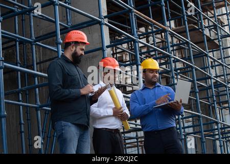 Männlicher Ingenieur mit Laptop und Gespräch mit seinen Kollegen, während er auf der Baustelle steht. Stockfoto