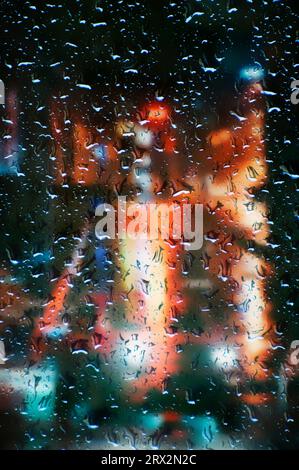 Fenster mit Regentropfen und verschwommener nächtlicher City-Szene dahinter Stockfoto