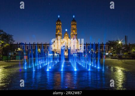 Zapopan Basilika, Guadalajara, Mexiko, beleuchtet von Scheinwerfern bei Nacht und von farbigen Wasserfontänen im Vordergrund. Stockfoto