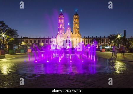 Zapopan Basilika, Guadalajara, Mexiko, beleuchtet von Scheinwerfern bei Nacht und von farbigen Wasserfontänen im Vordergrund. Stockfoto