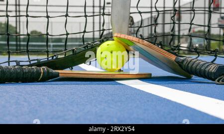 Ein kleiner Blickwinkel auf die Nahaufnahme von zwei Pickleball-Paddles auf einem gelben Schlagball am Netz auf einem Platz Stockfoto