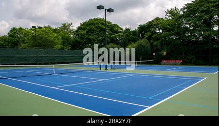Blick über den Innenhof auf Tennisplätze mit Pickleball, blau und grün gestrichen, mit Lichtern und Bäumen im Hintergrund. Stockfoto