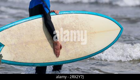 Mann in blauem und schwarzem Neoprenanzug, der sein Surfbrett auf Gilgo Beach Long Island ins Meer trägt. Stockfoto