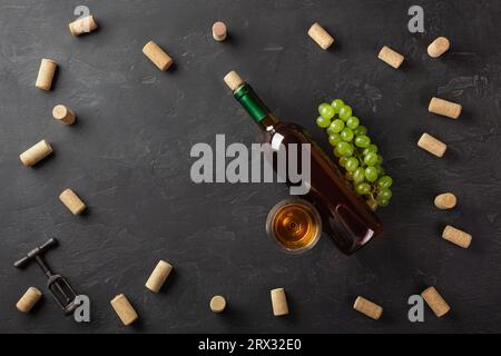 Weiße Flasche Wein, Trauben und Weinglas mit Korken und Korkenzieher auf schwarzem Hintergrund. Ansicht von oben mit der Kopie. Stockfoto