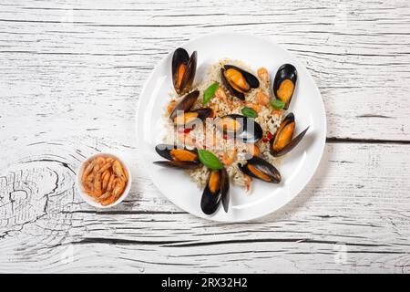 Gebratener Reis mit Muscheln, Shrimps und Basilikum auf einem Teller auf einem weißen Holztisch. Draufsicht. Stockfoto
