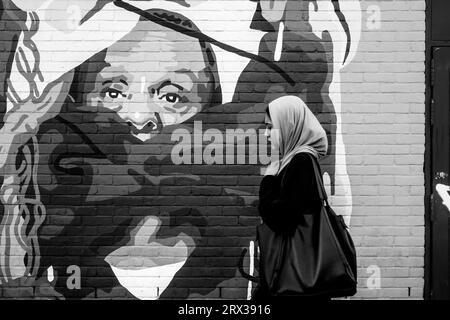 Eine junge Frau spaziert vorbei an farbenfroher Street Art, Shoreditch, London, UK. Stockfoto