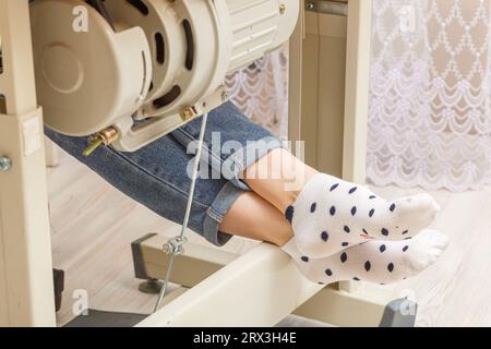 Weibliche Füße auf dem Pedal einer Nähmaschine, Nahaufnahme des Motors Stockfoto