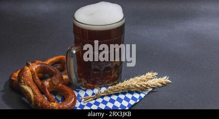 Traditionelles Oktoberfest. Brezeln und Bier, deutsches Festivalkonzept. Trendiges hartes Licht, dunkler Schatten, dunkler Steinbetonhintergrund, Banner f Stockfoto