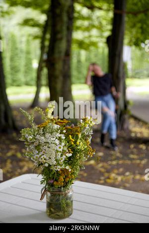 Ein Strauß wilder Blumen in einem Glas vor dem Hintergrund einer verschwommenen Silhouette einer Frau auf einer Schaukel Stockfoto