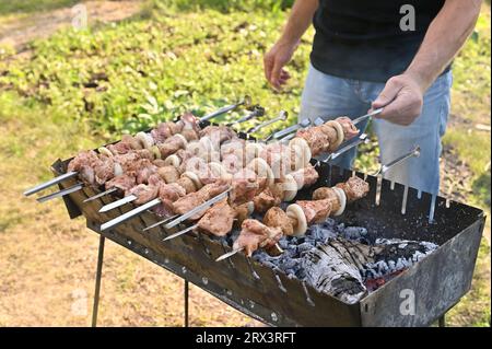 Ein Mann dreht einen Spieß mit einem Grill auf dem Grill um Stockfoto