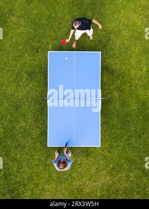 Die Leute, die draußen Tischtennis spielen, sehen sich aus der Vogelperspektive an. Blick von oben zwei Jungs spielen Tischtennis auf einem grünen Rasen. Outdoor-Sport aus der Vogelperspektive Stockfoto