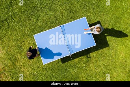 Die Leute, die draußen Tischtennis spielen, sehen sich aus der Vogelperspektive an. Blick von oben zwei Jungs spielen Tischtennis auf einem grünen Rasen. Outdoor-Sport aus der Vogelperspektive Stockfoto