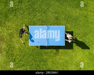 Die Leute, die draußen Tischtennis spielen, sehen sich aus der Vogelperspektive an. Blick von oben zwei Jungs spielen Tischtennis auf einem grünen Rasen. Outdoor-Sport aus der Vogelperspektive Stockfoto