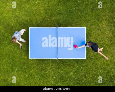 Die Leute, die draußen Tischtennis spielen, sehen sich aus der Vogelperspektive an. Blick von oben zwei Jungs spielen Tischtennis auf einem grünen Rasen. Outdoor-Sport aus der Vogelperspektive Stockfoto