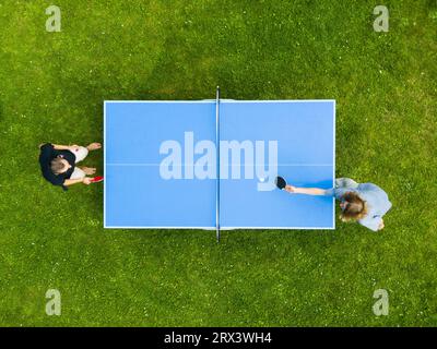 Die Leute, die draußen Tischtennis spielen, sehen sich aus der Vogelperspektive an. Blick von oben zwei Jungs spielen Tischtennis auf einem grünen Rasen. Outdoor-Sport aus der Vogelperspektive Stockfoto