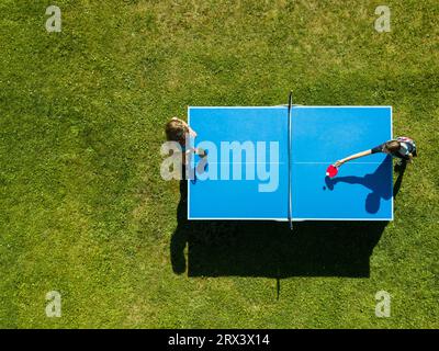 Die Leute, die draußen Tischtennis spielen, sehen sich aus der Vogelperspektive an. Blick von oben zwei Jungs spielen Tischtennis auf einem grünen Rasen. Outdoor-Sport aus der Vogelperspektive Stockfoto