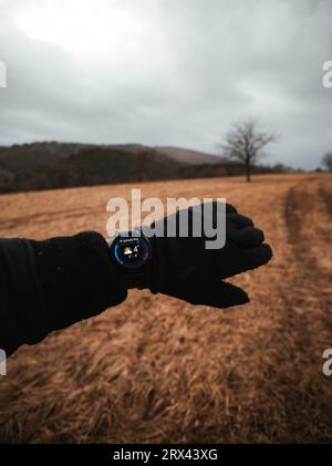 POV-Ansicht eines Mannes mit Winterhandschuhen, der auf seine Smarthuhren auf der linken Hand schaut und das Wetter überprüft. Mann in der Natur mit Smartwatches am Handgelenk im Sieg Stockfoto
