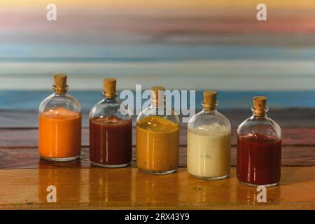 Handgemachte scharfe Saucen in Glasflaschen mit Kork auf farbigem Holzsockel - Salsas picantes hechas artesanalmente en botellas de vidrio con corcho Sob Stockfoto