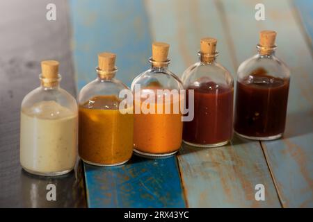 Handgemachte scharfe Saucen in Glasflaschen mit Kork auf farbigem Holzsockel - Salsas picantes hechas artesanalmente en botellas de vidrio con corcho Sob Stockfoto