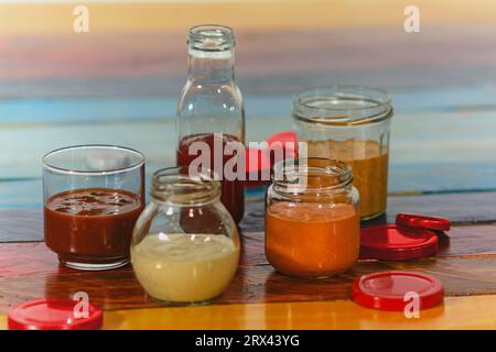 Handgemachte scharfe Saucen in Gläsern auf farbigem Holzsockel - Salsas picantes hechas artesanalmente en frascos de vidrio sobre fondo de madera de Col Stockfoto