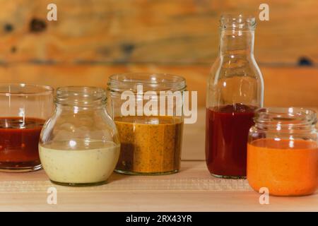 Handgemachte scharfe Saucen in Gläsern auf farbigem Holzsockel - Salsas picantes hechas artesanalmente en frascos de vidrio sobre fondo de madera de Col Stockfoto