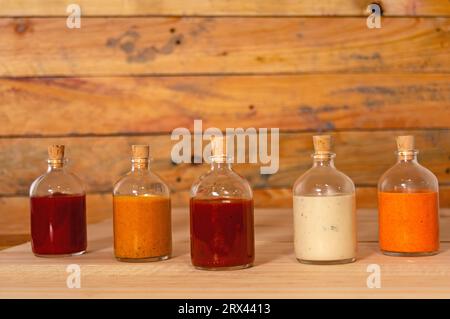 Handgemachte scharfe Saucen in Glasflaschen mit Kork auf farbigem Holzsockel - Salsas picantes hechas artesanalmente en botellas de vidrio con corcho Sob Stockfoto