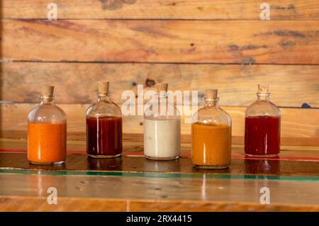 Handgemachte scharfe Saucen in Glasflaschen mit Kork auf farbigem Holzsockel - Salsas picantes hechas artesanalmente en botellas de vidrio con corcho Sob Stockfoto