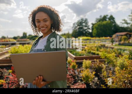 Gärtnerin, die am Laptop arbeitet, während sie auf dem Hintergrund des Shopplants Centers sitzt Stockfoto