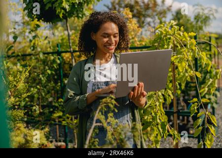 Gärtnerin, die am Laptop arbeitet, während sie auf dem Hintergrund des Shopplants Centers steht Stockfoto