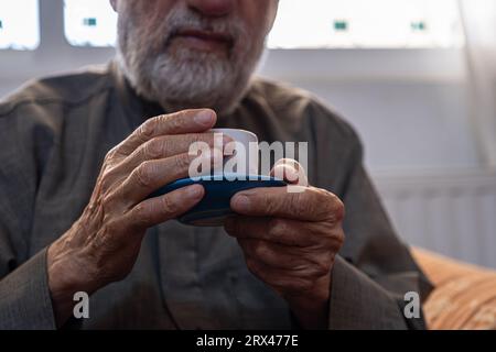 Der alte Mann trinkt Kaffee mit einem Lächeln im Gesicht Stockfoto
