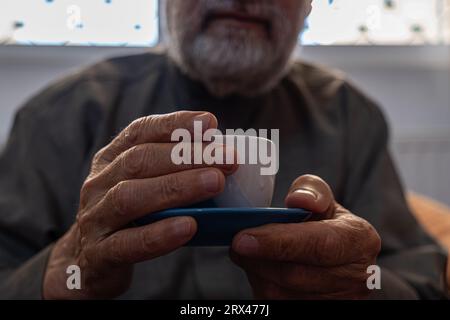 Der alte Mann trinkt Kaffee mit einem Lächeln im Gesicht Stockfoto