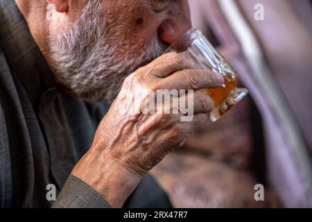 Arabischer alter Mann trinkt Tee und hält ein Glas Tee in der Hand Stockfoto