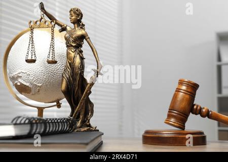 Figur der Lady Justice, Hammer, Notizbücher und Globus auf dem Tisch drinnen, Platz für Text. Symbol der gerechten Behandlung nach dem Gesetz Stockfoto