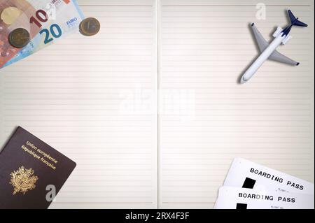 Ein französischer Pass, zwei Flugtickets, ein Spielzeugflugzeug und einige Euro auf einem Notizblock mit Kopierplatz. Stockfoto