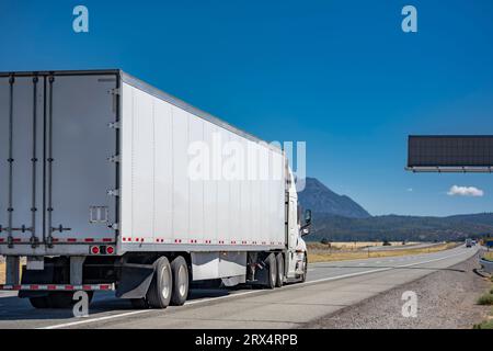 Industrieller langer Transportträger, weißer Großwagen-Sattelzugmaschine, der gewerbliche Fracht in einem trockenen Transporter transportiert, der auf der geraden Achse läuft Stockfoto