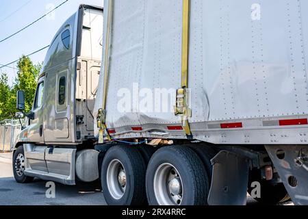 Beigefarbener Großfahrzeug-Sattelzugwagen in Industriequalität mit gebrochenem, trockenem Transporter-Auflieger, der mit einer Schlinge befestigt ist, die auf der Straße der Stadt steht und auf das mögliche wartet Stockfoto