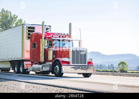 Industrieller langer Transportträger, roter klassischer Großfahrzeug-Sattelzugmaschine mit verlängerter Kabine für Lkw-Fahrerlager, der Fracht im Kühlschrankteil transportiert Stockfoto