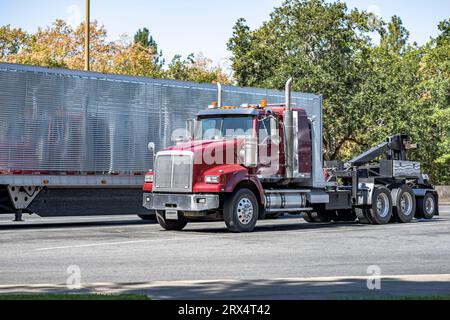 Industrieller leistungsstarker burgunderroter Straßenhelfer mobiler, großer Lkw, der einen Auflieger mit Hubausleger abschleppt, der auf dem Stapler steht, hält Parken lo an Stockfoto