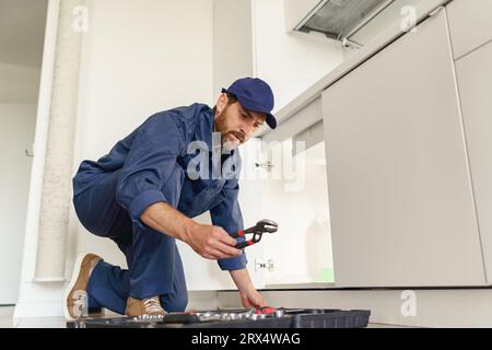 Professioneller Klempner nimmt einen verstellbaren Schraubenschlüssel aus der Werkzeugtasche für die Reparatur von Rohren Stockfoto