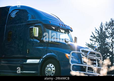 Blauer Industrieträger, großer Lkw-Sattelzugmaschine mit Hochleistungsrohren, Kühlergrillschutz und Blendung durch die Sonnenstrahlen auf der Karosserie, die auf der Autobahn läuft r Stockfoto