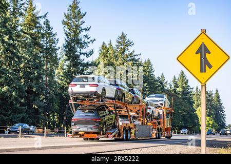 Leuchtend orangefarbener Industriestandard-Autotransporter, klassischer Träger, großer Auflieger, Sattelzugmaschine für den Transport von Autos, zweistufiger hydraulischer, modularer Auflieger, dri Stockfoto