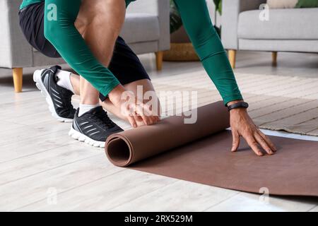 Sportlicher Reifer Mann, der sich zu Hause die Fitnessmatte ausrollen lässt, Nahaufnahme Stockfoto