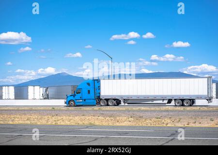 Industrietauglicher beladener langer Transportträger, blauer Großfahrzeug-Sattelschlepper, der gewerbliche Fracht in einem trockenen Transporter transportiert, der auf dem Hochplateau fährt Stockfoto