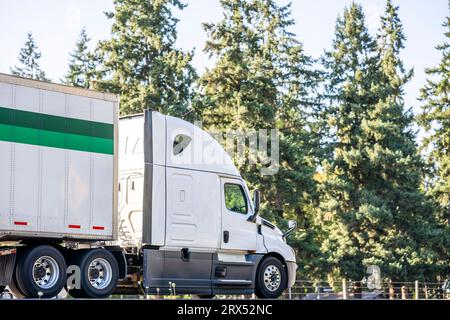 Industrieller beladener, langer Transportträger, weißer, großer Lkw-Sattelschlepper, der gewerbliche Fracht in einem trockenen Transporter transportiert, der auf der Höhe läuft Stockfoto