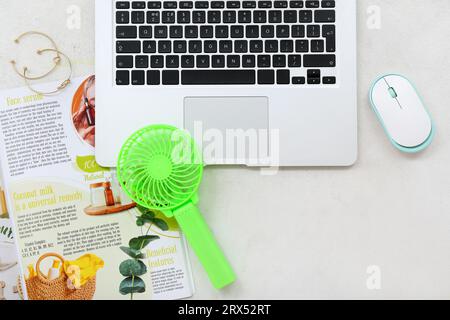 Tragbarer grüner Elektroventilator, Laptop und Magazin auf weißem Grunge-Hintergrund Stockfoto