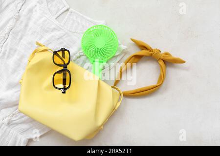 Tragbarer grüner Elektroventilator, Tasche und weibliche Kleidung auf weißem Grunge-Hintergrund Stockfoto