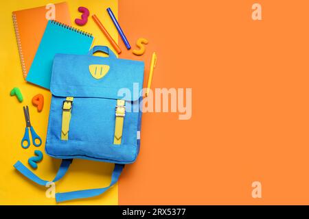Stylischer Schulrucksack mit verschiedenen Schreibwaren auf farbigem Hintergrund Stockfoto